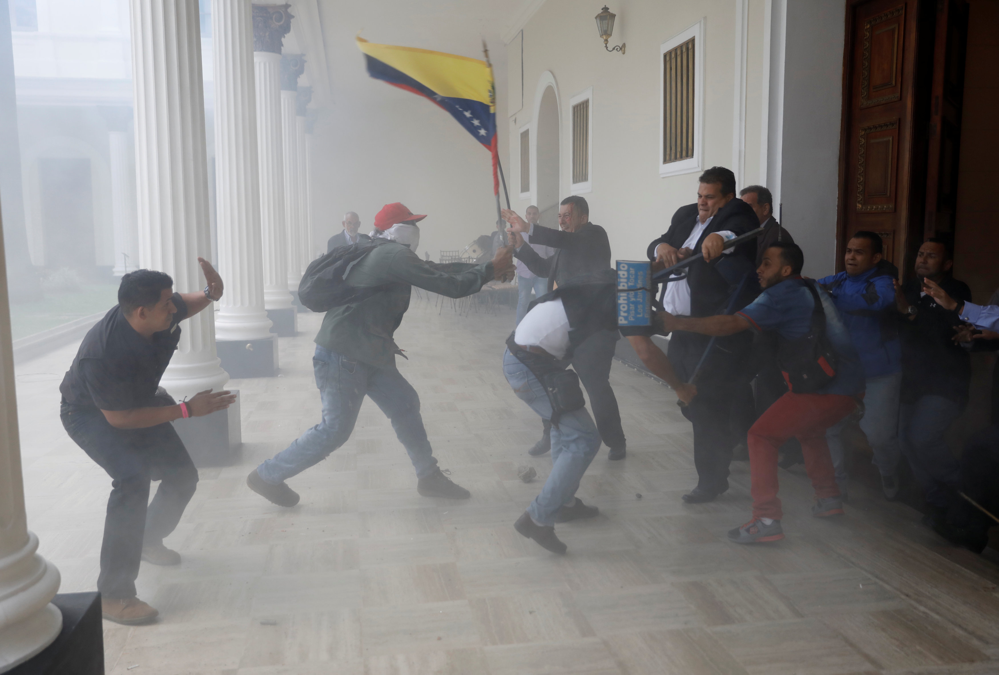 A goverment supporter holds a National flag while clashing with people outside Venezuela's opposition-controlled National Assembly, in Caracas